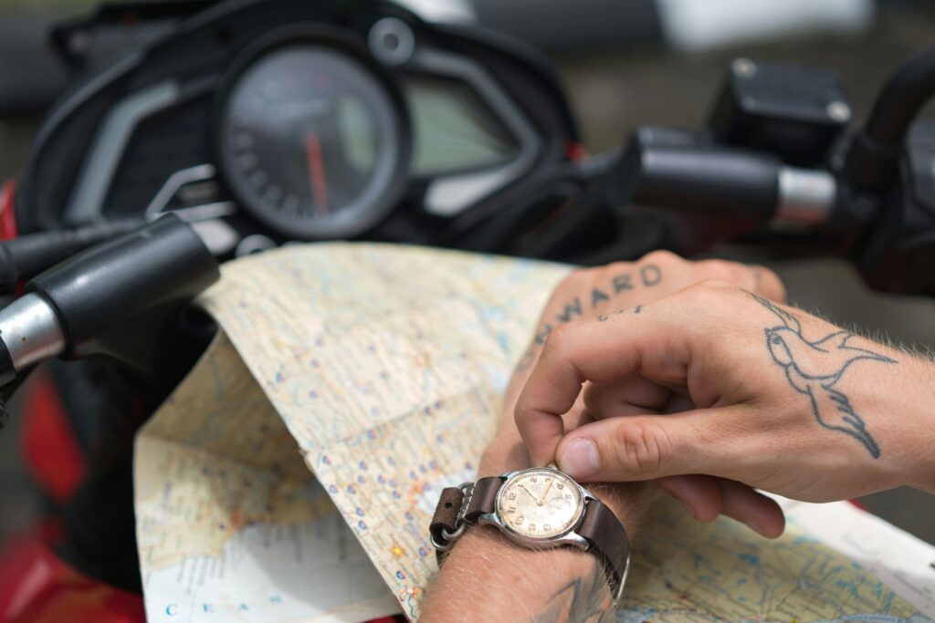 Motorradfahrer prüft eine Landkarte auf dem Tank seines Motorrads, mit einem tätowierten Pfeil auf dem Handrücken, der symbolisch "vorwärts" weist